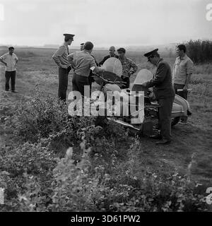 UdSSR, Ukrainische SSR, Slavyanogorsk (Svyatogorsk), 1970er Jahre Eine freimütige Szene in einem Feld in der Nähe des Resorts mit sowjetischen Militsiya-Offizieren und Anwohnern. Eine Gruppe von Männern versammelt sich mit einem Beiwagen um ein Motorrad. Ein Offizier schreibt ein Dokument, während ein anderer bereit ist. Die Zivilisten in lässigen Kleidern reden und rauchen; ein Mann lächelt in die Kamera. Der Hintergrund zeigt Schilf und ferne Hügel. Dieses archivierte Schwarzweiß-Foto zeigt ein Stück ländliches Leben im friedlichen Donbass. Stockfoto