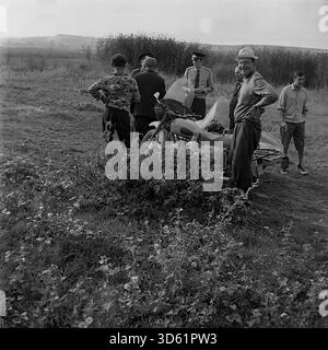 UdSSR, Ukrainische SSR, Slavyanogorsk (Svyatogorsk), 1970er Jahre Eine freimütige Szene in einem Feld in der Nähe des Resorts mit sowjetischen Militsiya-Offizieren und Anwohnern. Eine Gruppe von Männern versammelt sich mit einem Beiwagen um ein Motorrad. Ein Offizier schreibt ein Dokument, während ein anderer bereit ist. Die Zivilisten in lässigen Kleidern reden und rauchen; ein Mann lächelt in die Kamera. Der Hintergrund zeigt Schilf und ferne Hügel. Dieses archivierte Schwarzweiß-Foto zeigt ein Stück ländliches Leben im friedlichen Donbass. Stockfoto