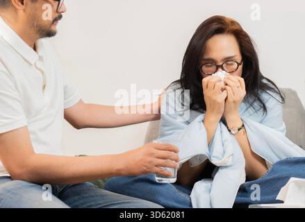 Gutaussehender Mann, der sich um seine kranke Freundin kümmert, während er zu Hause auf dem Sofa sitzt. Medikation und Gesundheitskonzept Stockfoto