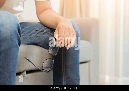 Er versuchte den jungen Mann auf dem Sofa auszuruhen und litt unter Augenanstrengung. Er nahm die Brille ab. Augenschmerzen, Leiden, Überlastung Burnout Stress von Lon Stockfoto