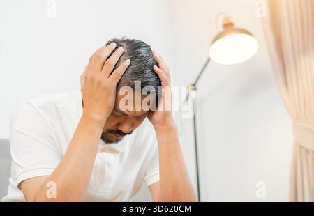 Verärgerter unglücklicher erwachsener Mann, der den Kopf mit den Händen zusammendrückt und an Kopfschmerzen leidet. Mensch, Stress, Spannung und Migräne Stockfoto