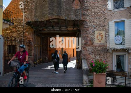 Italien, Borghetto - 2. Oktober 2025: Touristen gehen durch einen Steinbogen in die charmanten mittelalterlichen Gassen des Dorfes, umgeben von rustikalen Stockfoto