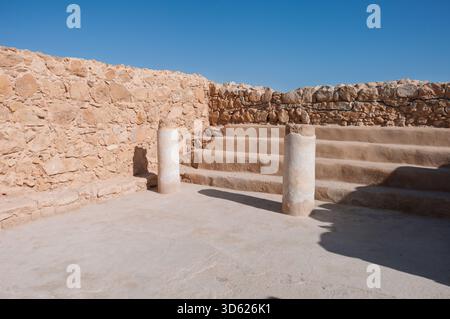Eine Steinmauer mit zwei Säulen in der Mitte. Die Säulen befinden sich in der Mitte eines Hofes mit einer Steintreppe. Der Innenhof ist leer und der Himmel ist leer Stockfoto