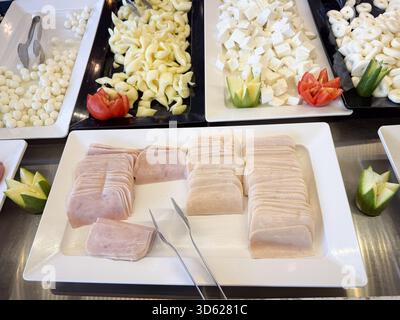 An einem Buffet werden verschiedene Käsesorten und aufgeräumte Wurstscheiben mit Gemüsegarnituren präsentiert Stockfoto