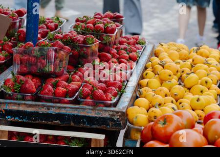 Frische, reife Erdbeeren, gelbe Loquats und Tomaten auf einem Straßenmarkt. Farbenfrohe saisonale Früchte in Plastikbehältern im Freien angeordnet Stockfoto