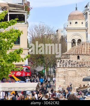 Athen, Griechenland - 15. Mai 2024: Touristen und Einheimische auf einem belebten Platz mit historischer Kirche und Sightseeing Bus Stockfoto