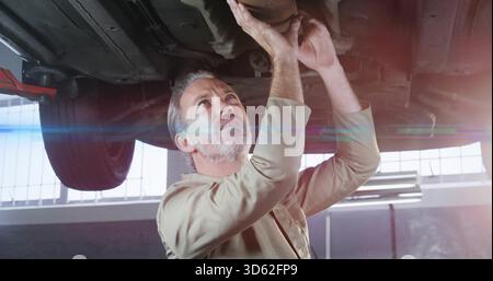 Mechaniker im braunen Hemd, der den Auspuff unter dem Fahrzeug auf dem Aufzug in der Garage hält, Hinterrad sichtbar Stockfoto