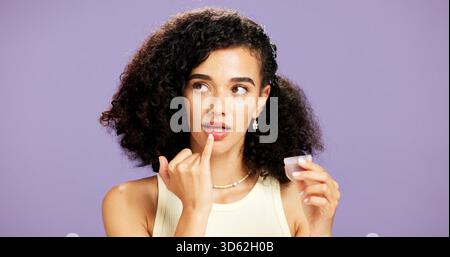 Frau, Schönheit und Lippengloss mit Produkt im Kosmetikstudio auf lila Hintergrund. Weibliche Person, Modell oder Lippenstift mit Behälter für auftragen Stockfoto