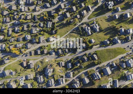 Aus der Vogelperspektive auf Dächer und gewundenen Straßen entsteht ein strukturierter Wandteppich, eingebettet in Grünflächen, eine harmonische Mischung aus urbanen und natürlichen Elementen, Va Stockfoto