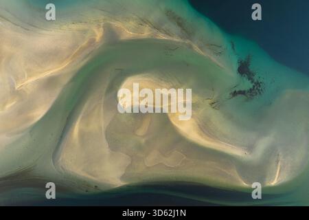 Aus der Vogelperspektive sehen Sie das türkisfarbene Wasser, das auf goldenen Sand trifft, ein Tanz aus Licht und Schatten, der ätherische Muster auf der Leinwand der Küste, Isafjordu, erzeugt Stockfoto