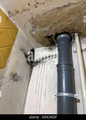 Das Innere eines Wohnhauses weist schwere Wasserschäden, feuchte Flecken und Schimmel an der Decke und den Wänden um eine schlecht abgedichtete PVC-Rohrleitung auf. Vernachlässigung, Infrastrukturausfall, Probleme bei der Hausverwaltung. Stockfoto