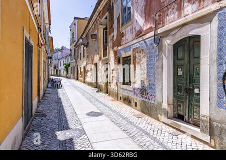 Eine bezaubernde, sonnendurchflutete Kopfsteinpflasterallee im historischen Zentrum von Tomar, Portugal, mit alten Gebäuden mit verblassten Fliesen und einer grünen Holztür. Stockfoto