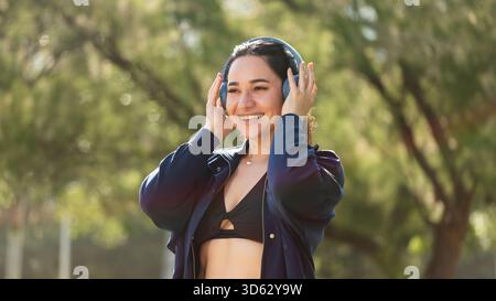Eine junge Frau, die unsichtbare kieferorthopädische Aligner trägt, lächelt glücklich und hört Musik mit ihren Kopfhörern Stockfoto