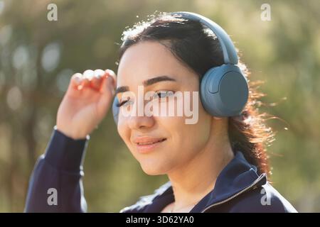 Eine Frau entspannt sich und genießt die Musik, die sie mit ihren Kopfhörern hört, während sie im Park spaziert und trainiert Stockfoto