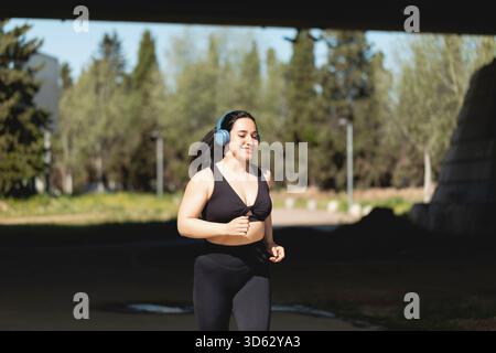 Eine starke junge Frau spielt Sport und läuft fröhlich im Park, hört Musik mit Kopfhörern Stockfoto