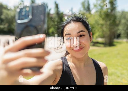Eine junge Frau lächelt entspannt, während sie ein Selfie mit dem Handy macht, um hübsch auszusehen, nachdem sie Sport gemacht hat Stockfoto