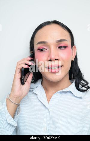 Studio-Porträt eines jungen thailändischen Transgender mit Make-up und langen Haaren. Das Konzept des Geschlechterausdrucks, des LGBTQ-Stolzes und der Inklusivität zeigt eine Stockfoto