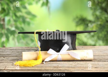 Graduierungskappe und Diplom auf Holztisch vor verschwommenem Hintergrund, Nahaufnahme. Leerzeichen für Text Stockfoto