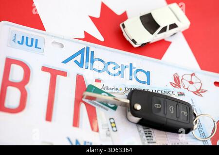 Alberta canadian Autokennzeichen und Zündschlüssel auf der Flagge von Kanada Nahaufnahme. Führerschein- und Zulassungskonzept Stockfoto