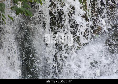 Dynamische Nahaufnahme von tropfenden Wasserfalltröpfchen, die in Bewegung gefroren sind und natürliche Texturen, Energie und den lebhaften Kontrast zwischen Wasser und Moos freigeben Stockfoto