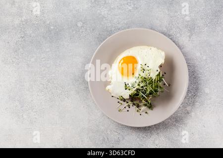 Traditionelles englisches Frühstück mit Spiegeleiern mit Rucola microgreen in grauer Keramikplatte auf grauem Beton altem Hintergrund. Draufsicht. Stockfoto