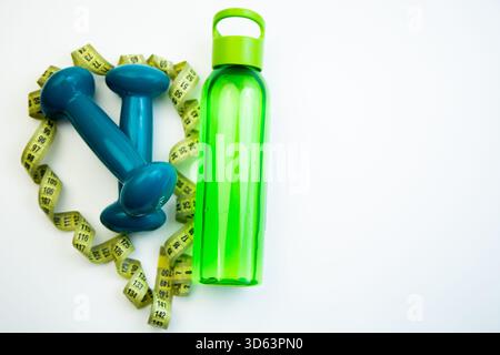Lebendige Kurzhanteln und eine grüne Wasserflasche sind kreativ in Herzform mit Messung angeordnet Stockfoto