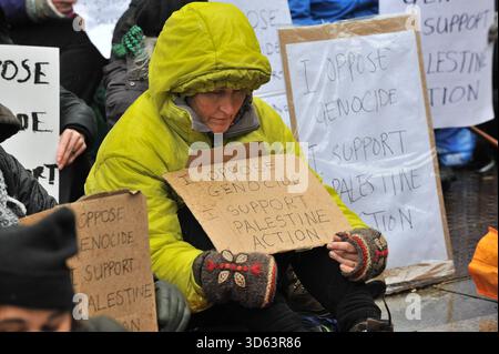 EDINBURGH, SCHOTTLAND: 18. November 2025: Demonstranten sitzen mit Plakat. Am 18. November 2025 versammelten sich Demonstranten vor dem Queen Elizabeth House in Edinburgh als Teil der landesweiten „Lift the Ban“-Aktionen, die die britische Regierung gegen das Verbot der Palästinensischen Aktion als terroristische Organisation anfechten. Demonstranten sitzen still und halten Schilder mit der Aufschrift „Ich bin gegen Völkermord. Ich unterstütze die Palästinensische Aktion“, während Mitglieder der schottischen palästinensischen Solidaritätskampagne T-Shirts mit der Aufschrift „Völkermord in Palästina“ tragen. Zeit, Maßnahmen zu ergreifen.“ Quelle: Eastern Goodwin Media/Alamy Live News Stockfoto