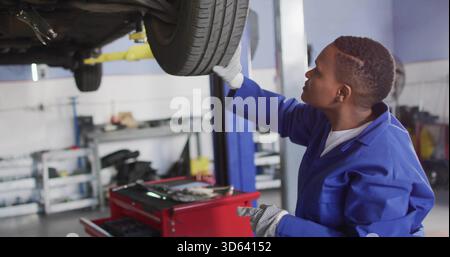 Inspektion des Mechanikers in blauem Overall, Überprüfung des Fahrzeugrads im Aufzug mit Handschuhen, Kopierraum Stockfoto