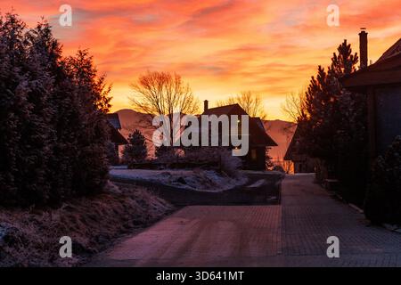 Frostiges Bergdorf mit hölzernen Hütten, die im orange Sonnenaufgangslicht leuchten, und frostbedeckten Bäumen. Stockfoto