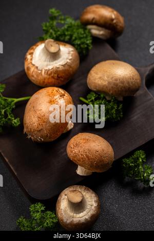 Braune Cremini-Pilze und frische grüne Petersilienblätter auf einem rustikalen dunklen Holzschneidebrett, die gesunde Bio-Zutaten für Co hervorheben Stockfoto