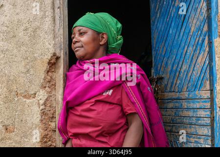 Gasura Ruanda - 8. September 2025; Afrikanerin in traditioneller, farbenfroher Kleidung aus rotem und rosa Rock und Wickel mit grünem Kopftuch stehend i Stockfoto