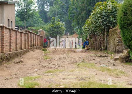 Gasura Ruanda - 8. September 2025; Ziegelmauer, die entlang einer Feldstraße in einem afrikanischen Dorf mit Menschen in der Ferne führt Stockfoto