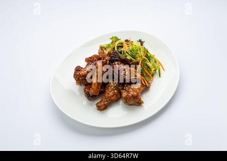 Glasierte Hähnchenflügel mit Sesam und frischem Krautsalat auf weißem Teller, Blick vom Studio von oben Stockfoto