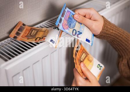 Ein Mädchen in einem Pullover zählt Geld bei einem Heizkörper: 50 und 20 Euro, eine Nahaufnahme von 20 Euro. Das Zimmer ist kalt, was den Bedarf an Heizung unterstreicht. Hallo Stockfoto