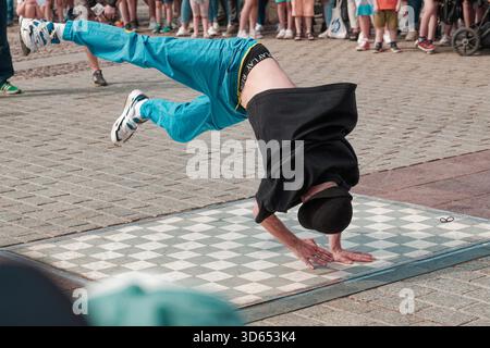 Breakdancer von Kraków B-Boys Familia führt während einer hochenergetischen Straßenaufführung ein inverses Einfrieren durch, während das Publikum zusieht. Stockfoto