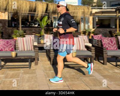 Mann in sportlicher Kleidung, der an einem sonnigen Tag an der Can pastilla mallorca spanien vorbei an einem Lounge-Bereich im Freien mit gepolsterten Sitzgelegenheiten und tropischem Dekor joggt Stockfoto