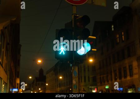 Fußgängersignal leuchtet grün vor dunkler Stadtkulisse mit historischen Gebäuden und Straßenfahrten Stockfoto