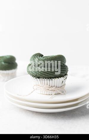 Grüner Frosting mit Schokoladenchips auf Cupcakes mit weißem Hintergrund, Cupcakes in weißen Linern mit hohem Buttercremewirl, grüner Buttercremefrost Stockfoto