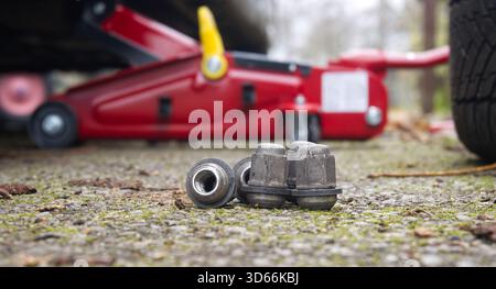 Werkzeuge für die automatische Wartung sitzen auf einer rauen Oberfläche und verfügen über einen roten hydraulischen Wagenheber und lose Radmuttern. Die Reparaturszene im Freien deutet auf eine Fahrzeugwartung hin Stockfoto