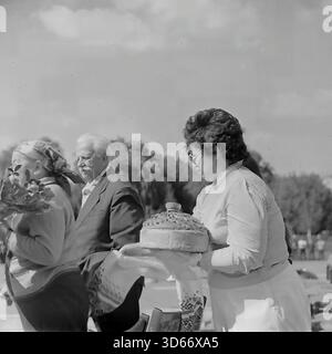 Slawjansk, Ukraine, UdSSR - 8. September 1985: Authentisches Archivfoto einer traditionellen Ehrungszeremonie während des Stadttages. Eine Frau präsentiert einem älteren Paar auf der Bühne einen zeremoniellen Brotlaib (Korovai) auf einem gestickten Handtuch. Die Veteranen halten Blumen. Dieses Schwarzweiß-Bild zeigt den tiefen slawischen Brauch der Gastfreundschaft und des Respekts für die ältere Generation, der während eines Feiertags in der Donezker Region in der Sowjetzeit gezeigt wurde. Stockfoto
