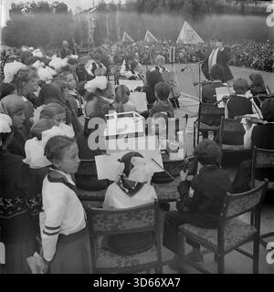 Slawjansk, Ukraine, UdSSR - 8. September 1985: Atmosphärisches Archivfoto, aufgenommen von der Bühne während des Stadtfestes. Ein männlicher Dirigent führt ein Streichorchester für Kinder, das für eine riesige Menge von Bürgern spielt, die sich auf dem Platz versammelt haben. Im Vordergrund sieht eine Gruppe von Mädchen mit großen weißen Bögen den Auftritt. Das Schwarzweiß-Bild fängt das Ausmaß des Feiertags und das kulturelle Leben der Donezker Region in der friedlichen Sowjetzeit ein. Stockfoto