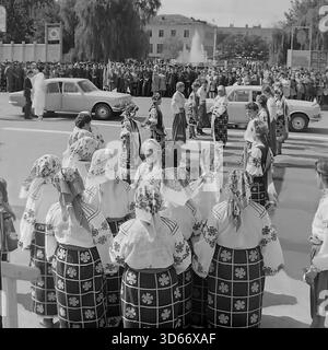Slawjansk, Ukraine, UdSSR - 8. September 1985: Historisches Archivfoto des Stadtfestes auf dem zentralen Platz. Ein Volkstanz-Ensemble in traditionellen ukrainischen Kostümen begrüßt das Brautpaar, das in einem dekorierten Wolga-Auto ankommt. Das Schwarzweiß-Bild zeigt eine feierliche Zeremonie mit einer Braut und einem Bräutigam während einer öffentlichen Großveranstaltung. Im Hintergrund sind eine große Menschenmenge und ein Brunnen zu sehen, die die kulturellen Traditionen der Donezker Region in der Sowjetzeit widerspiegeln. Stockfoto