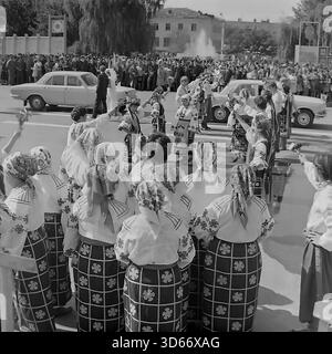 Slawjansk, Ukraine, UdSSR - 8. September 1985: Historisches Archivfoto des Stadtfestes auf dem zentralen Platz. Ein Volkstanz-Ensemble in traditionellen ukrainischen Kostümen begrüßt das Brautpaar, das in einem dekorierten Wolga-Auto ankommt. Das Schwarzweiß-Bild zeigt eine feierliche Zeremonie mit einer Braut und einem Bräutigam während einer öffentlichen Großveranstaltung. Im Hintergrund sind eine große Menschenmenge und ein Brunnen zu sehen, die die kulturellen Traditionen der Donezker Region in der Sowjetzeit widerspiegeln. Stockfoto