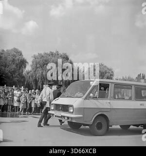 Slawjansk, Ukraine, UdSSR - 8. September 1985: Dokumentarisches Archivfoto während der Feierlichkeiten zum Stadttag. Ein sowjetischer Minibus der RAF-2203 'Lettland' fährt langsam durch den Platz, begleitet von einem Milizoffizier in Uniform, der die Menge kontrolliert. Die Zuschauer stehen im Hintergrund in der Nähe großer Weiden. Dieses Schwarzweiß-Bild fängt die authentische Straßenatmosphäre, den sowjetischen Verkehr und die Maßnahmen der öffentlichen Ordnung in der Region Donezk während der friedlichen Ära ein. Stockfoto