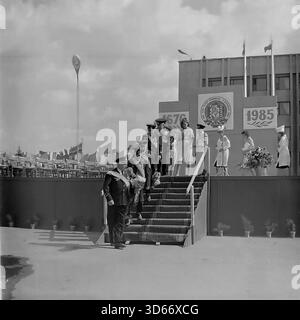 Slawjansk, Ukraine, UdSSR - 8. September 1985: Großes Archivfoto der Zeremonie zum Stadttag auf dem zentralen Platz. Eine Gruppe von Ehrenbürgern in Uniformen mit Schärpen und Blumen steigt die Treppe von der Hauptbühne hinab, die mit dem Stadtwappen verziert ist und datiert von 1676 bis 1985. Frauen in weißen Mänteln stehen auf der Plattform. Das Bild fängt die feierliche Atmosphäre, die Größe der Dekoration und den Respekt vor Veteranen in der Region Donezk während der friedlichen Sowjetzeit ein. Stockfoto
