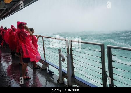 Touristen in nassen rosa Regenponchos stehen am Geländer des Niagara City Cruises Tourbootes, während sie im Nebel am Fuße der Horseshoe Falls liegen Stockfoto