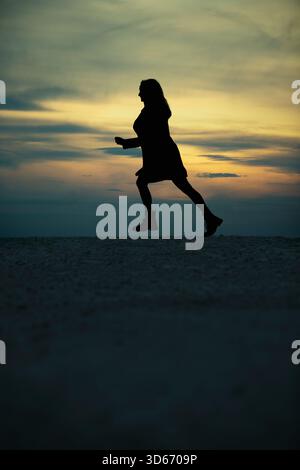 Seitenansicht Silhouette in voller Länge Frauenfigur, die gegen Sonnenuntergang läuft Stockfoto