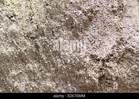 Nahaufnahme von grobem Sand in Kombination mit verschiedenen kleinen Steinen, die natürliche Texturen und Farben bei hellem Sonnenlicht zeigen. Stockfoto