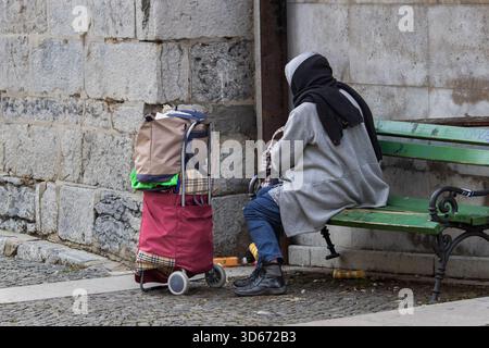 Ljubljana, Slowenien 19. Oktober 2025 Frau, die auf einer Bank mit Karren in der Nähe einer Steinmauer sitzt Stockfoto