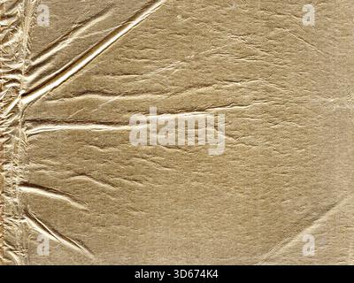 Strukturiertes Goldpapier mit zerknitterter Oberfläche. Das reflektierende Material sorgt für ein glänzendes, metallisches Erscheinungsbild mit horizontalen und vertikalen Falten Stockfoto